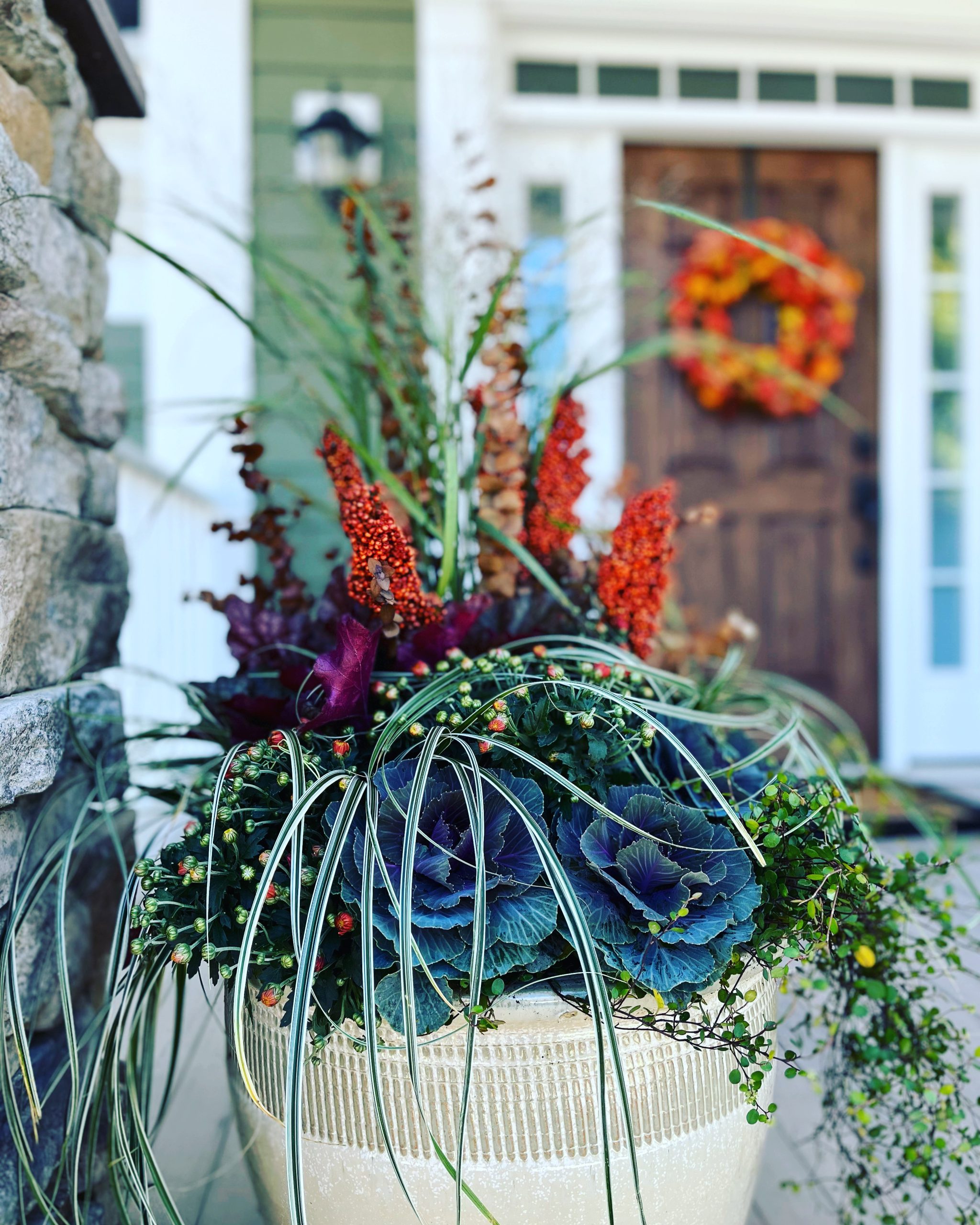 Large white ceramic planter with fall vegetation sits outside a home